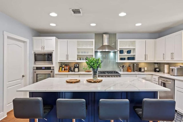 611 W Johanna St, Austin, TX 78704 - kitchen featuring stainless steel appliances, open shelves, wall chimney range hood, a kitchen breakfast bar, and white cabinetry