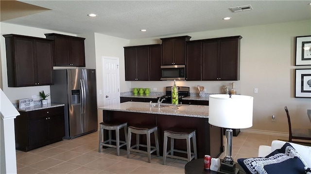 10909 Mickelson Dr, Austin, TX 78747 - kitchen with stainless steel appliances, dark brown cabinets, light tile patterned flooring, a kitchen island with sink, and recessed lighting