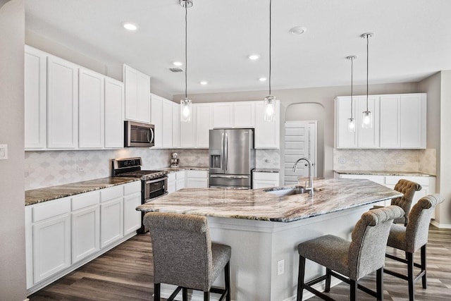 1805 Bogata Ln, Leander, TX 78641 - kitchen with stainless steel appliances, dark wood-style floors, white cabinetry, a breakfast bar, and light stone counters
