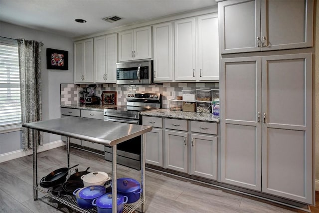 569 Mcallister Rd, Bastrop, TX 78602 - kitchen featuring stainless steel appliances, decorative backsplash, gray cabinetry, light wood-style flooring, and light stone countertops