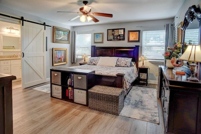 569 Mcallister Rd, Bastrop, TX 78602 - bedroom with a barn door, light wood finished floors, multiple windows, and connected bathroom