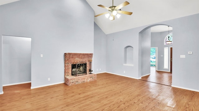 606 Dundalk Bay Cv, Pflugerville, TX 78660 - unfurnished living room with high vaulted ceiling, a ceiling fan, light wood-style floors, a brick fireplace, and arched walkways