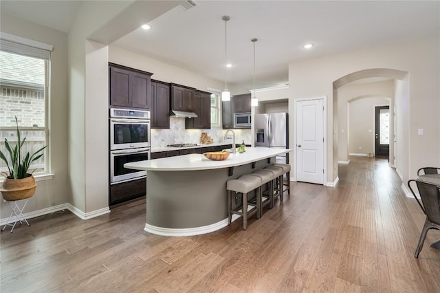 5612 Wild Foxglove Rd, Spicewood, TX 78669 - kitchen with appliances with stainless steel finishes, dark brown cabinets, light countertops, arched walkways, and a center island with sink