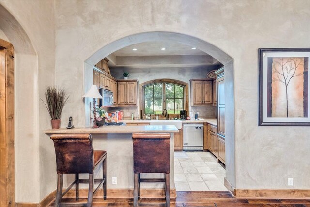 171 Oak Grove Cv, Georgetown, TX 78628 - kitchen featuring dishwashing machine, stainless steel microwave, light countertops, a peninsula, and a breakfast bar