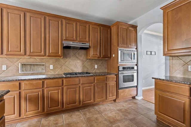 908 Golden Palomino Ct, Austin, TX 78732 - kitchen featuring stainless steel appliances, under cabinet range hood, arched walkways, brown cabinets, and crown molding