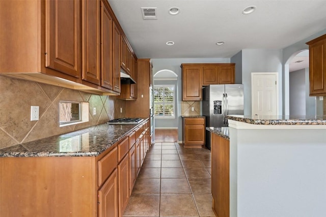 908 Golden Palomino Ct, Austin, TX 78732 - kitchen with arched walkways, dark stone counters, brown cabinetry, decorative backsplash, and appliances with stainless steel finishes