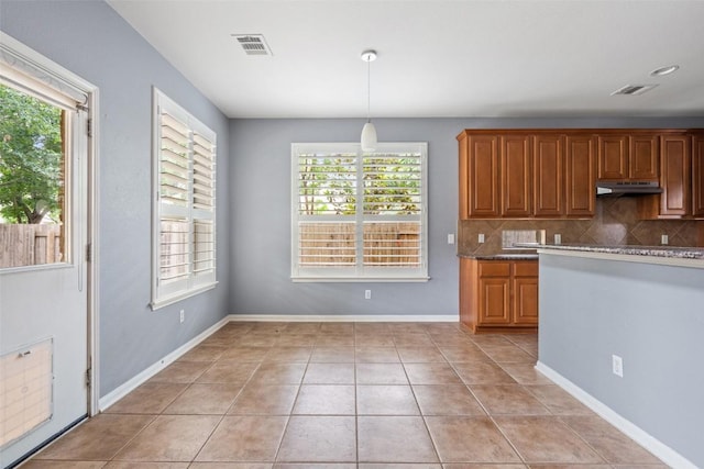 908 Golden Palomino Ct, Austin, TX 78732 - kitchen featuring backsplash, under cabinet range hood, brown cabinets, pendant lighting, and light tile patterned flooring