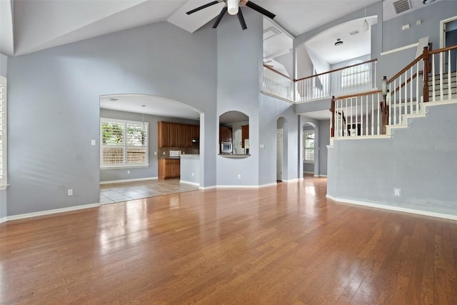 908 Golden Palomino Ct, Austin, TX 78732 - unfurnished living room featuring ceiling fan, high vaulted ceiling, arched walkways, light wood-type flooring, and stairway
