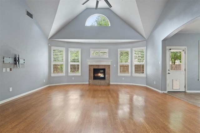 908 Golden Palomino Ct, Austin, TX 78732 - unfurnished living room featuring ceiling fan, a tile fireplace, wood finished floors, arched walkways, and high vaulted ceiling