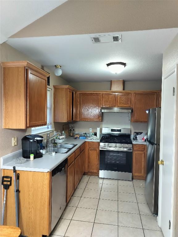 611 Clearcreek Dr, Leander, TX 78641 - kitchen featuring stainless steel appliances, under cabinet range hood, light countertops, light tile patterned flooring, and brown cabinets