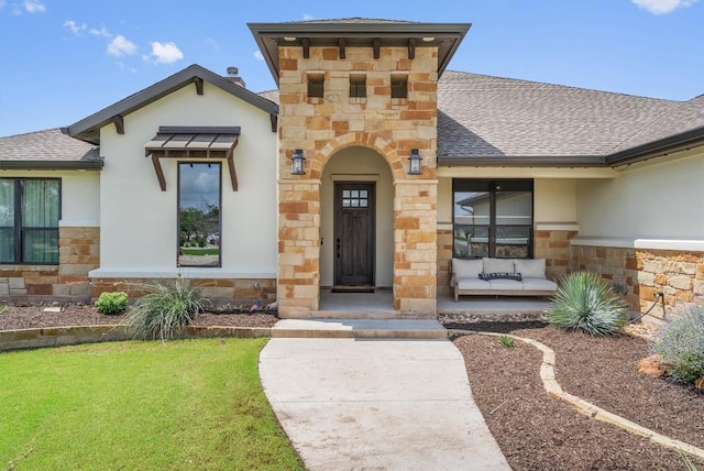 205 Honey Locust Cv, Leander, TX 78641 - view of exterior entry with stone siding, roof with shingles, stucco siding, a yard, and a porch