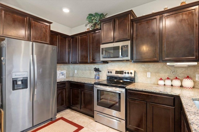212 Plata Ln, Jarrell, TX 76537 - kitchen with appliances with stainless steel finishes, dark brown cabinetry, light tile patterned floors, decorative backsplash, and light stone counters