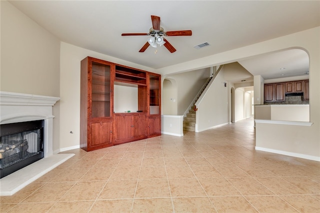 903 Fork Ridge Path, Round Rock, TX 78665 - unfurnished living room featuring arched walkways, ceiling fan, light tile patterned floors, a fireplace with raised hearth, and stairway