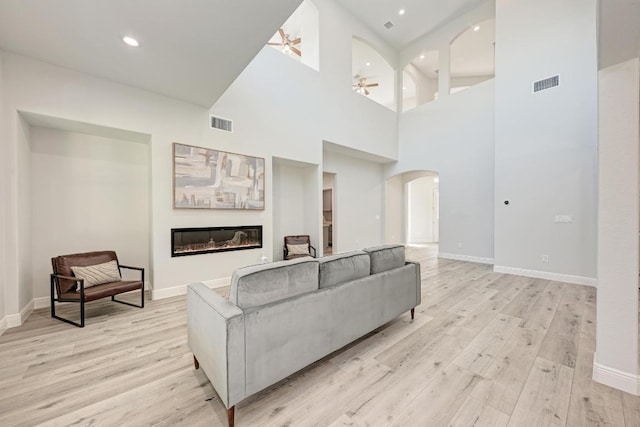13201 Mansfield Dr, Austin, TX 78732 - living area with arched walkways, a ceiling fan, a glass covered fireplace, light wood-style flooring, and recessed lighting