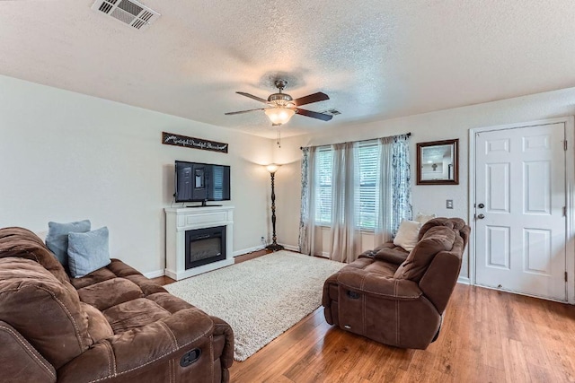 1229 Twin Cv, Kyle, TX 78640 - living room featuring a textured ceiling, light wood-type flooring, a ceiling fan, and a glass covered fireplace