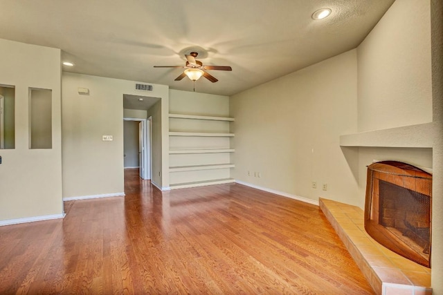 8200 Neely Dr Unit 116, Austin, TX 78759 - unfurnished living room with a ceiling fan, built in features, a tiled fireplace, wood finished floors, and recessed lighting