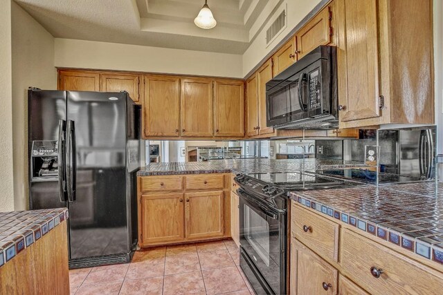 8200 Neely Dr Unit 116, Austin, TX 78759 - kitchen featuring black appliances, tile counters, a tray ceiling, light tile patterned floors, and brown cabinetry
