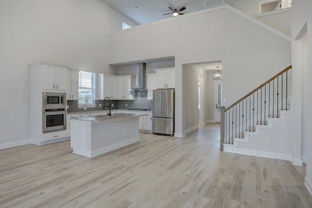 17212 Autumn Falls Dr, Manor, TX 78653 - kitchen featuring stainless steel appliances, wall chimney range hood, white cabinetry, light wood-style flooring, and a high ceiling