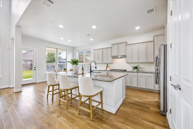 19612 Abigail Way, Pflugerville, TX 78660 - kitchen featuring stainless steel appliances, light stone countertops, a breakfast bar area, tasteful backsplash, and light wood-type flooring