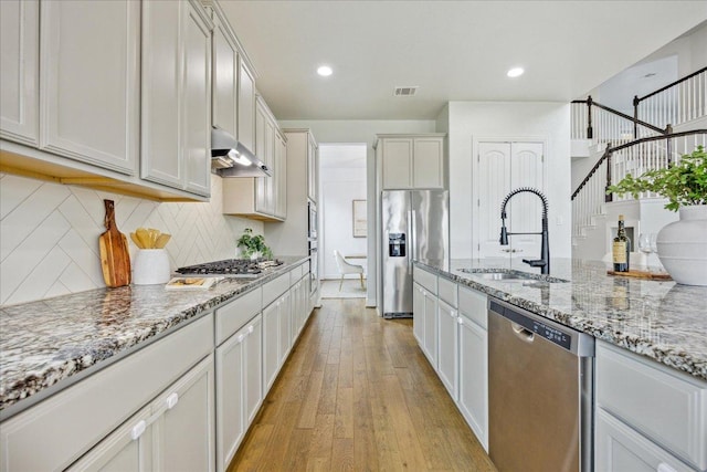 19612 Abigail Way, Pflugerville, TX 78660 - kitchen featuring appliances with stainless steel finishes, under cabinet range hood, decorative backsplash, light wood finished floors, and light stone counters