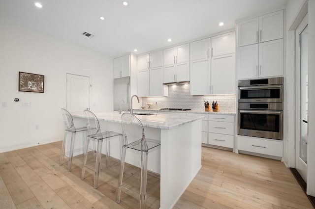 2608 Watkins Way, Austin, TX 78746 - kitchen with double oven, tasteful backsplash, light wood-type flooring, a kitchen island with sink, and recessed lighting