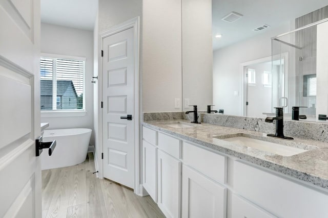 118 Periwinkle Ln, Bastrop, TX 78602 - full bath featuring double vanity, a shower stall, wood finished floors, a soaking tub, and plenty of natural light