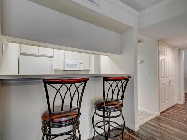 501 W 26th St Unit 102, Austin, TX 78705 - kitchen featuring white appliances, crown molding, wood finished floors, a kitchen breakfast bar, and white cabinets