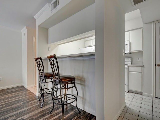 501 W 26th St Unit 102, Austin, TX 78705 - kitchen featuring white appliances, white cabinetry, a kitchen bar, wood finished floors, and ornamental molding