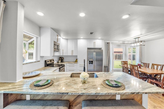 3705 Peach Vista Dr, Pflugerville, TX 78660 - kitchen featuring stainless steel appliances, light stone counters, a peninsula, a kitchen bar, and plenty of natural light