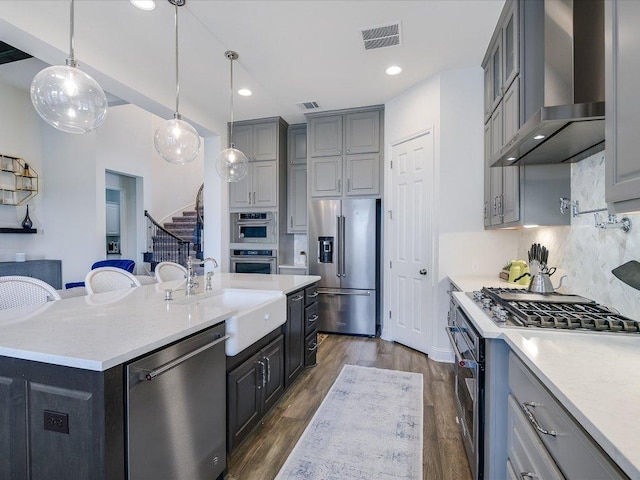 6701 Denia Dr, Austin, TX 78739 - kitchen featuring wall chimney exhaust hood, stainless steel appliances, an island with sink, tasteful backsplash, and gray cabinets