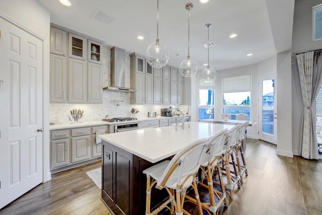 6701 Denia Dr, Austin, TX 78739 - kitchen with wall chimney range hood, light wood-type flooring, a large island, glass insert cabinets, and light countertops