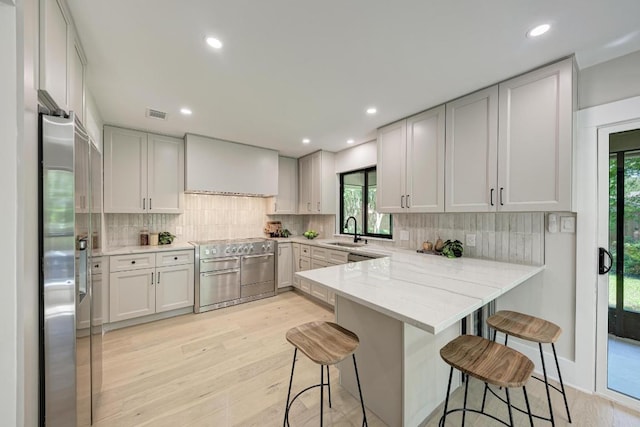 10507 Spicewood Pkwy, Austin, TX 78750 - kitchen with a peninsula, stainless steel appliances, light wood finished floors, a breakfast bar, and tasteful backsplash