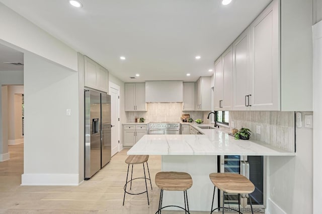 10507 Spicewood Pkwy, Austin, TX 78750 - kitchen featuring appliances with stainless steel finishes, a peninsula, wall chimney exhaust hood, light stone counters, and backsplash