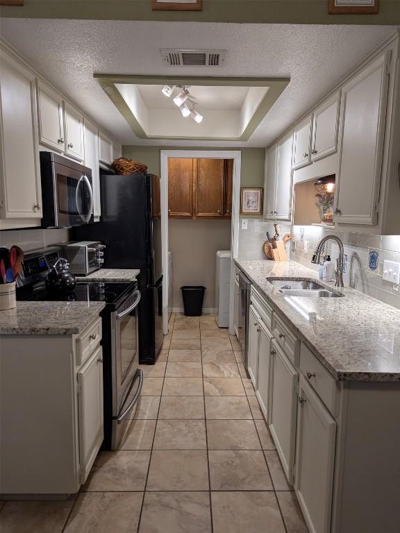 201 E Noton St Unit 105, Pflugerville, TX 78660 - kitchen featuring stainless steel appliances, a tray ceiling, light stone counters, a textured ceiling, and backsplash