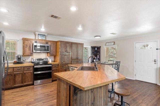 111 Lazy Trail Ct, Liberty Hill, TX 78642 - kitchen featuring stainless steel appliances, brown cabinetry, wood finished floors, a kitchen island with sink, and crown molding