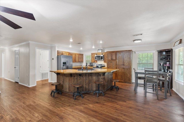 111 Lazy Trail Ct, Liberty Hill, TX 78642 - kitchen featuring appliances with stainless steel finishes, dark wood-style flooring, crown molding, brown cabinets, and a spacious island