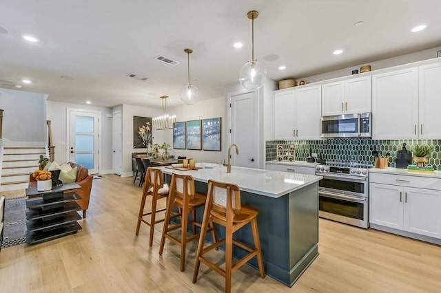 435 Emory Crossing Blvd, Hutto, TX 78634 - kitchen featuring appliances with stainless steel finishes, a center island with sink, backsplash, light countertops, and light wood-style flooring