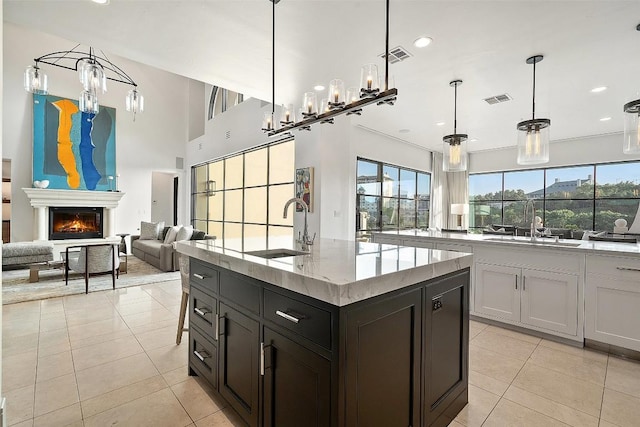 1508 Mesa Ridge Ln, Austin, TX 78735 - kitchen featuring light tile patterned flooring, light stone countertops, open floor plan, a center island with sink, and a warm lit fireplace