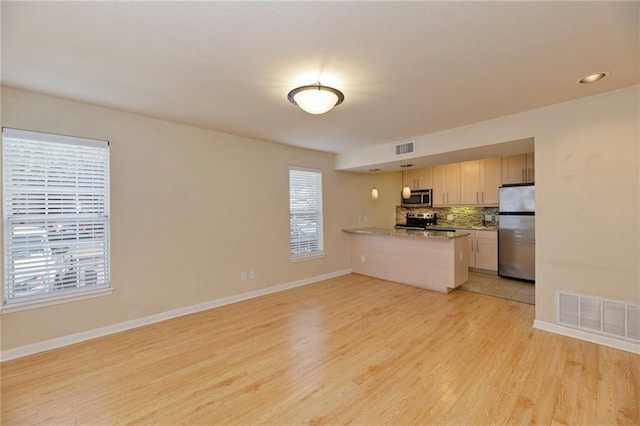 7685 Northcross Dr Unit 605, Austin, TX 78757 - kitchen featuring stainless steel appliances, a peninsula, light wood finished floors, tasteful backsplash, and pendant lighting