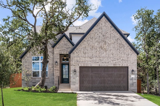 158 Loysoya St, Bastrop, TX 78602 - french country style house featuring driveway, an attached garage, a front yard, brick siding, and roof with shingles