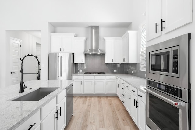 158 Loysoya St, Bastrop, TX 78602 - kitchen featuring stainless steel appliances, wall chimney exhaust hood, white cabinetry, light wood finished floors, and tasteful backsplash