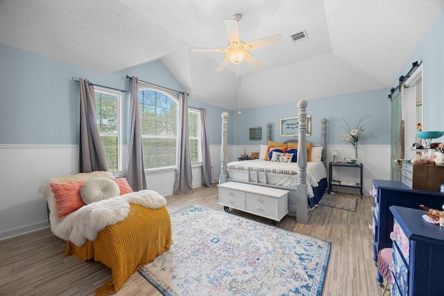 1306 River Oak Dr, Leander, TX 78641 - bedroom featuring wood finished floors, a textured ceiling, a barn door, lofted ceiling, and wainscoting