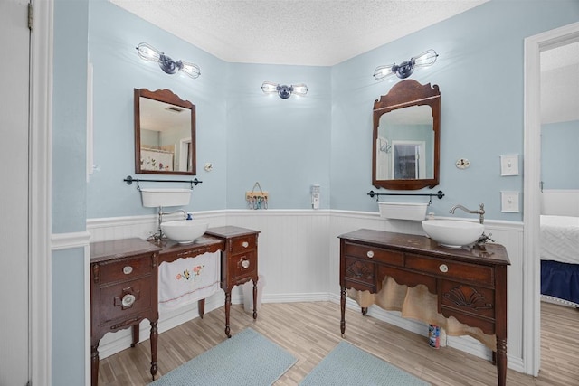 1306 River Oak Dr, Leander, TX 78641 - bathroom featuring wainscoting, a textured ceiling, two vanities, wood finished floors, and ensuite bath