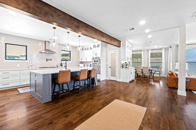 104 Hazeltine Dr, Georgetown, TX 78628 - kitchen featuring wall chimney exhaust hood, light countertops, a kitchen island with sink, white cabinets, and a breakfast bar