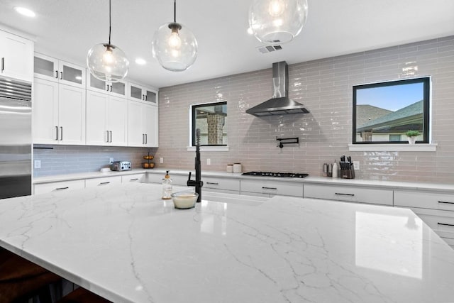 104 Hazeltine Dr, Georgetown, TX 78628 - kitchen featuring wall chimney range hood, built in refrigerator, backsplash, glass insert cabinets, and hanging light fixtures