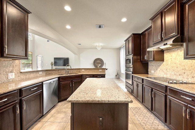 106 Tonkawa Trl W, Austin, TX 78738 - kitchen with stainless steel appliances, under cabinet range hood, a kitchen island, dark brown cabinetry, and light stone counters