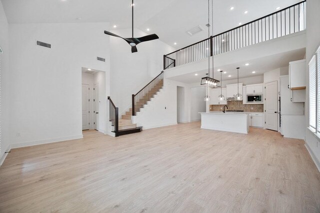 1601 Cardinal Ln, Round Rock, TX 78681 - unfurnished living room featuring a towering ceiling, light wood-style floors, stairs, ceiling fan, and recessed lighting