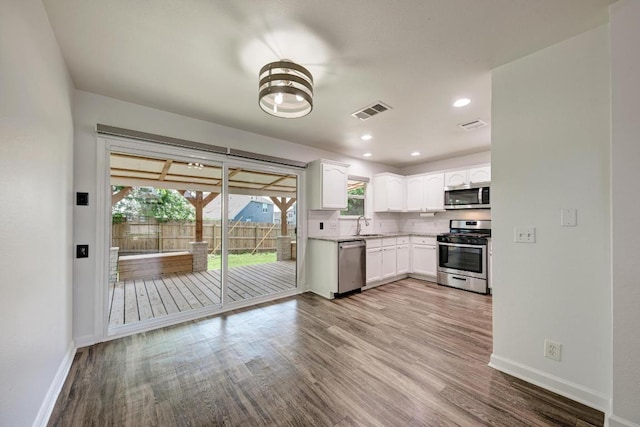 216 Cassandra Dr, Hutto, TX 78634 - kitchen featuring appliances with stainless steel finishes, wood finished floors, white cabinetry, decorative backsplash, and light countertops