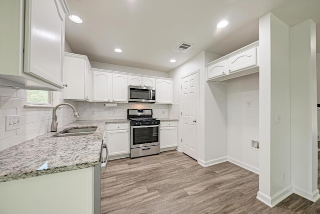 216 Cassandra Dr, Hutto, TX 78634 - kitchen with appliances with stainless steel finishes, light stone counters, light wood-type flooring, tasteful backsplash, and white cabinets