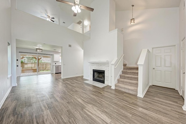 216 Cassandra Dr, Hutto, TX 78634 - unfurnished living room with a high ceiling, wood finished floors, a ceiling fan, a fireplace with flush hearth, and stairway